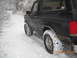1990 Ford Bronco - A black Ford Bronco drives down a snow-covered road in a wooded area.