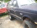 1990 Ford Bronco - A dark blue Ford Bronco sits next to a red and white truck, showing chains on its front tire.