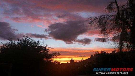 Sunset with colorful clouds over a silhouetted hill and trees. Watermark reads SUPERMOTORS