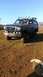 1995 Ford Bronco - A muddy Ford Bronco sits in a field under a clear blue sky, ready for off-road adventure.