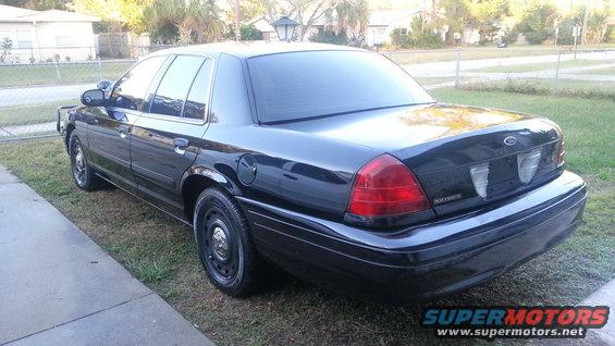 Black Ford Crown Victoria parked on grass next to a sidewalk