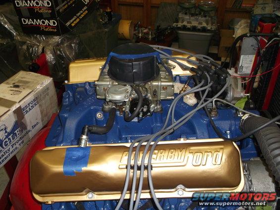 Ford V8 engine block painted blue, with gold valve covers reading "POWER BY FORD", carburetor, and spark plug wires