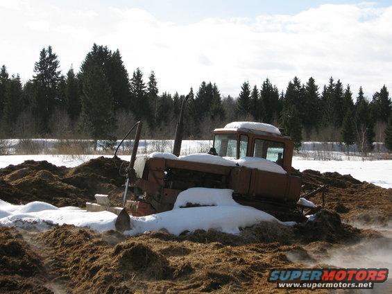 old tractor stuck in mud and snow, trees in background