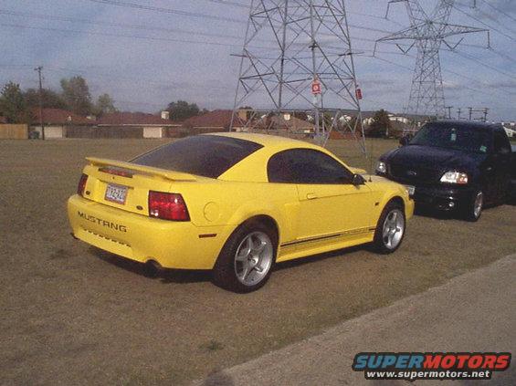 Yellow 2003 Ford Mustang parked next to a black pickup truck, with power lines overhead