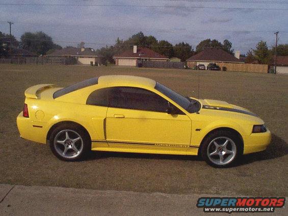 Yellow 2003 Ford Mustang GT coupe parked on grass, side view