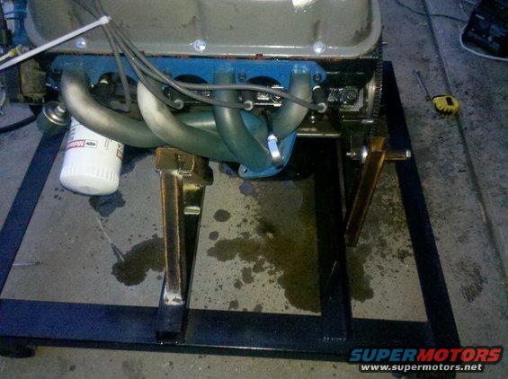 Engine on a stand with blue valve covers and silver exhaust manifolds, oil filter visible