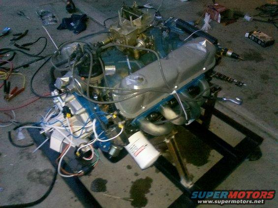 Engine assembly on a stand with wiring and a filter. Supermotors.net logo visible