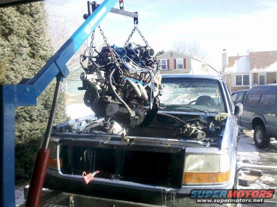 Truck with engine being lifted out by a blue engine hoist. Another truck is parked nearby