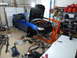 2007 Subaru Impreza - A blue 2007 Subaru Impreza is in a garage with its hood open and engine removed, surrounded by various car parts and tools.