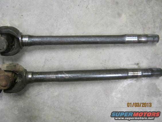 Two dark metal axle shafts with universal joints on a concrete surface