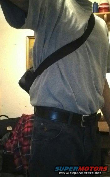 Person wearing a grey t-shirt, black belt, and dark jeans with a black bag strap across their chest
