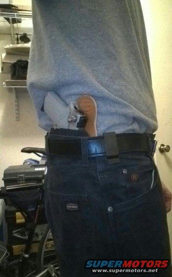 Holstered handgun with a wooden grip tucked into the waistband of dark denim jeans