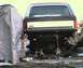 1984 Ford Bronco - The rear of a Ford Bronco is elevated on jack stands, undergoing work, with a tarp covering something to the left.