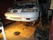 1992 Ford Taurus - A white sedan is raised on jack stands with its hood open, revealing the engine bay and a detached transmission nearby.