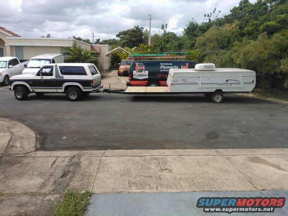 Side view of a black and white 1984 Ford Bronco towing a white pop-up camper