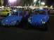 1970 Volkswagen Beetle - Two blue Volkswagen Beetles are parked next to each other under bright lights at night.