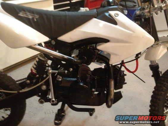 Dirt bike with white body panels and black seat. Engine and suspension visible