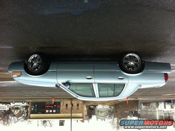 2003 Mercury Grand Marquis sedan, light blue, chrome wheels, parked on wet asphalt