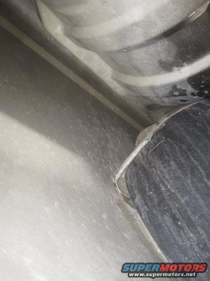 Close-up view of the underbody of a vehicle, showing a black cylindrical component and part of the frame