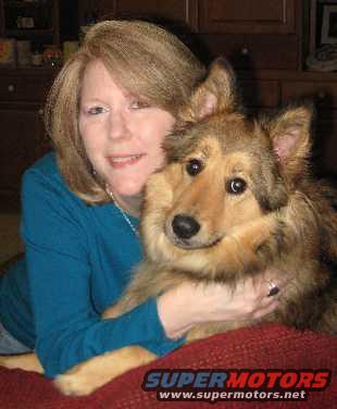 Woman in blue shirt holding a dog, with furniture in the background