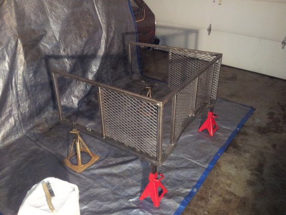 Metal cage frame on jack stands, covered by tarps in a garage