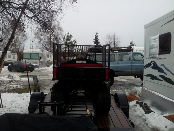 Trailer carrying an ATV, with a blue SUV and RVs in the background