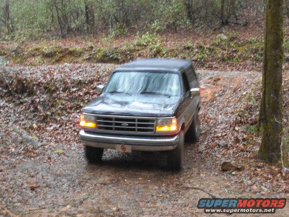 Dark SUV driving on a dirt road, front view. The vehicle has a grille with horizontal bars and rectangular headlights