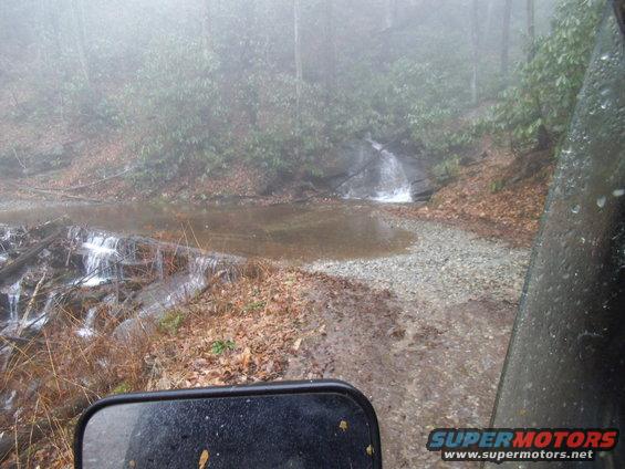 Side view mirror and vehicle door in foggy forest scene with stream crossing