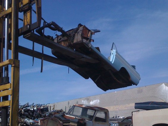 1964 Ford Ranchero body being lifted by forklift at junkyard