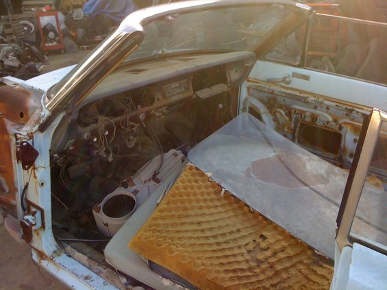Interior of a disassembled car, showing exposed wiring, rusted door panels, and loose seat cushions