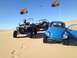 1970 Volkswagen Beetle - A blue Volkswagen Beetle and two off-road vehicles are parked on a sandy dune under a clear blue sky.