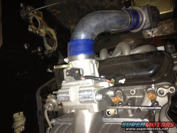 Close-up of a silver throttle body with a blue silicone coupler and gray intake tube attached to an engine