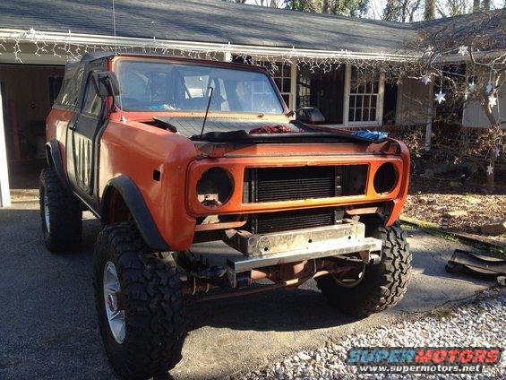 Orange SUV with black soft top, missing headlights and grille, lifted on large tires