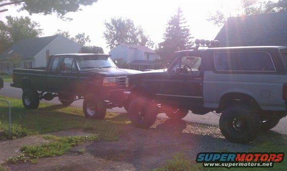 Two lifted trucks parked side-by-side, a dark pickup and a two-tone SUV