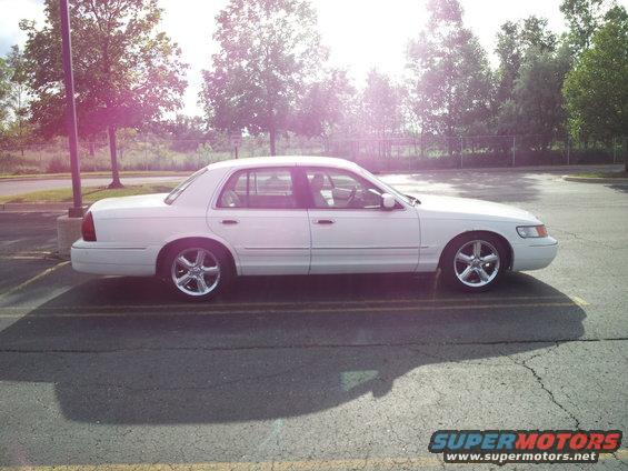 White sedan parked in a lot, side view. Looks like a 2000 Mercury Grand Marquis