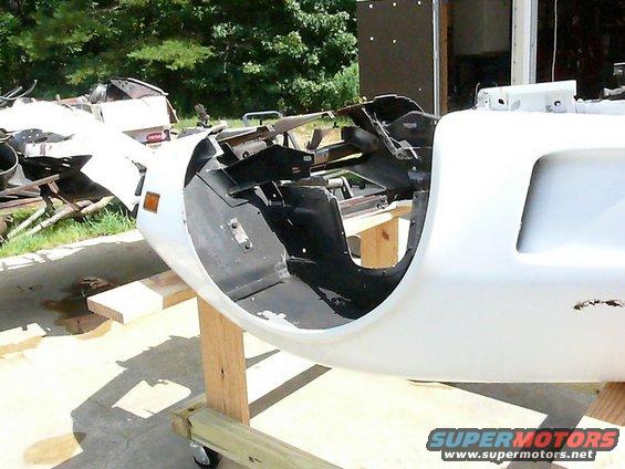 car front end disassembled on stand, showing internal structure. Some other car parts in background