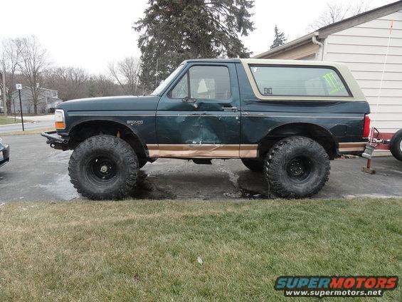 Dark green Ford Bronco with tan trim, lifted suspension, and large off-road tires, seen from the side