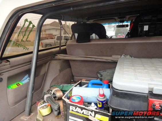 Interior view of a vehicle's cargo area with a roll cage, straps, and a toolbox. Monster Energy stickers are on the rear window