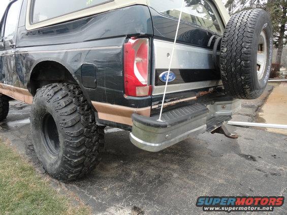 Dark green Ford Bronco rear quarter panel with a spare tire mounted on the back, tan trim, and large off-road tires