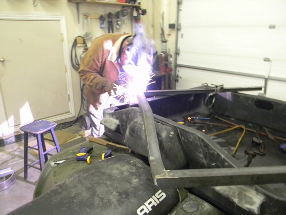 Guy welding metal frame onto an ATV in a garage. Text 'ARIS' visible on ATV