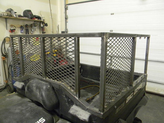 Utility vehicle with a custom metal cage, rear view. The vehicle has black plastic body panels and a metal grate cage