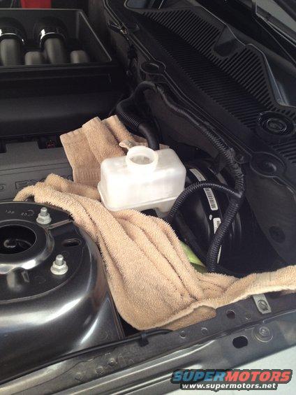 Under the hood, a brake fluid reservoir is covered by a towel. The engine bay of a 2013 Ford Mustang is visible