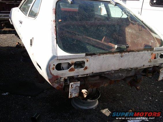 White car's rusty rear end with missing taillights, supported by a wheel rim