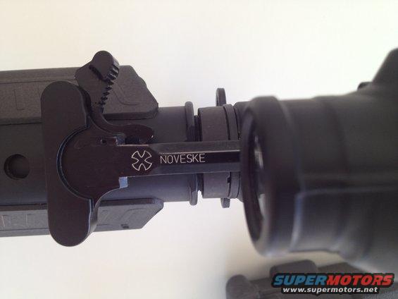 Close-up of a black AR-15 charging handle with the Noveske logo and name etched on it