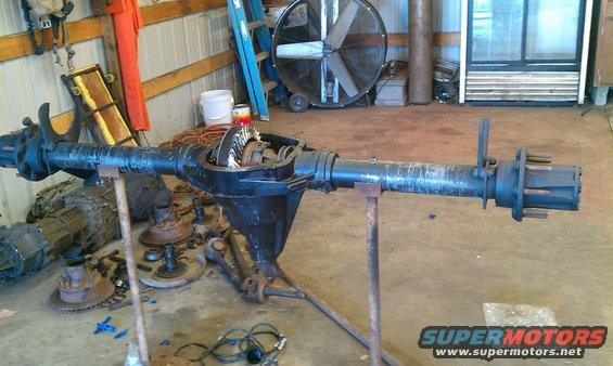 Differential axle assembly on stands, showing gears and axle shafts. Other parts and tools in background