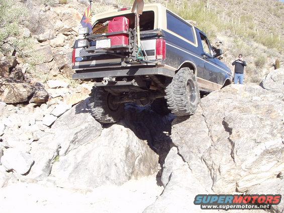 1993 Ford Bronco navigating a rocky trail, rear view, with spare tire and gas cans mounted
