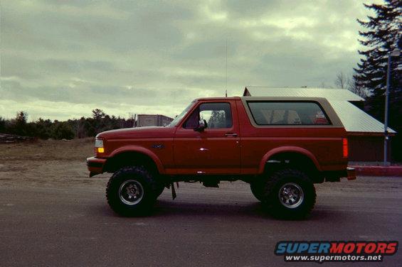 Red Ford Bronco parked on asphalt, side view. Lifted suspension, off-road tires