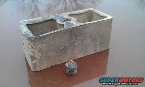 Metal part with two openings and a small cap on a reflective surface