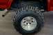 1995 Ford Bronco - Close-up of the rear tire and suspension of a red 1995 Ford Bronco, aggressive off-road tires.