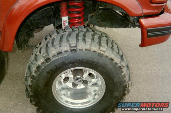 Close-up of a large off-road tire with a red shock absorber and coil spring visible